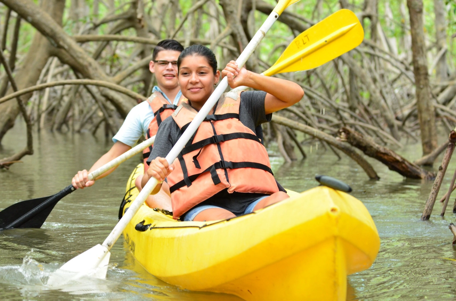 Dos visitantes remando en kayak amarillo entre las raíces de mangle del estuario Isla Damas cerca de Manuel Antonio, Costa Rica