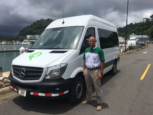 Chofer de Tucanes Tours junto a una microbús Mercedes blanca en la marina de Quepos, Costa Rica